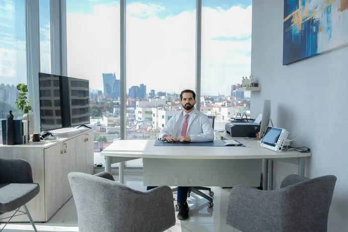 Dr. Nicholas Flores Flores en su escritorio, con vista panorámica de la ciudad